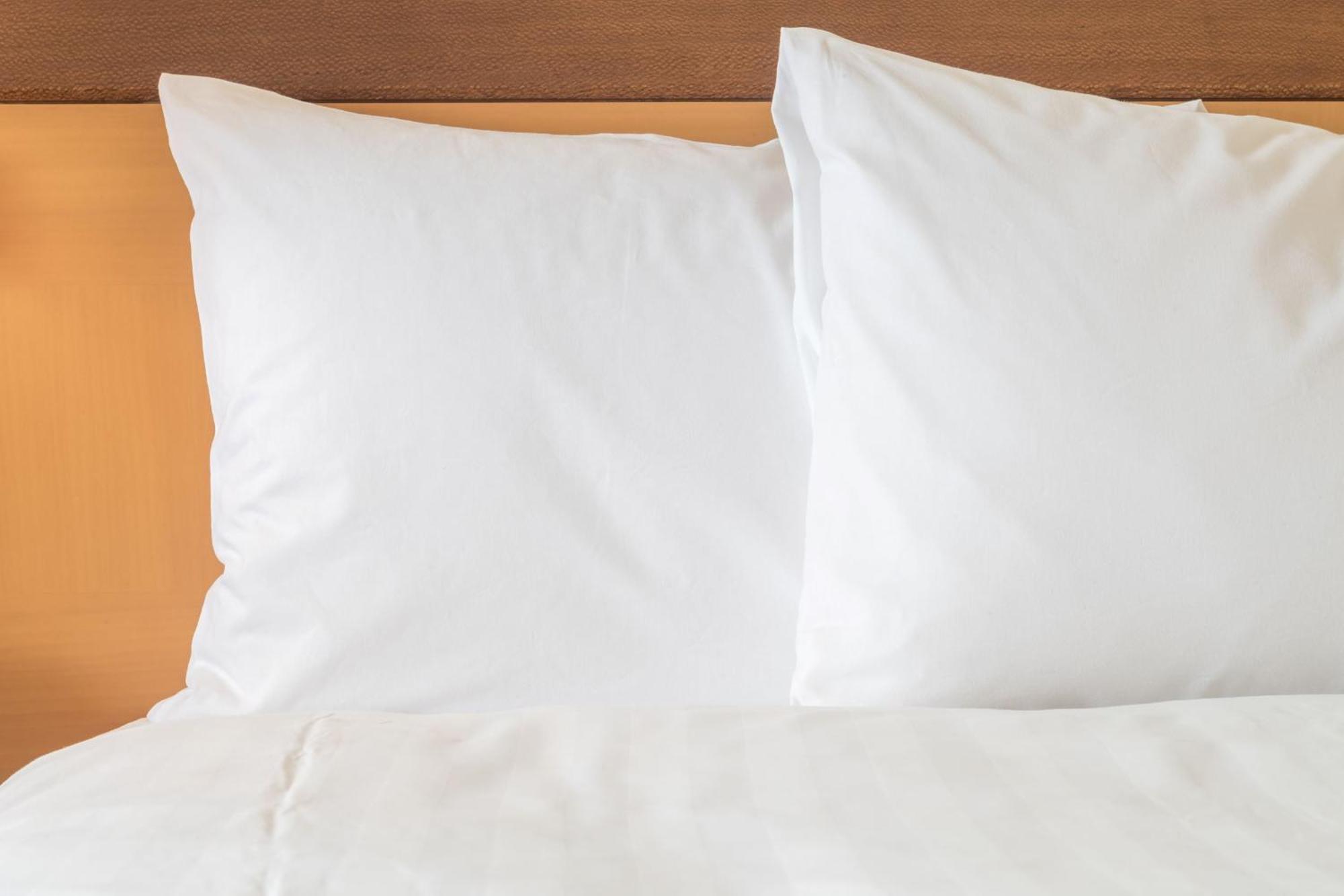 Dar Al Tawhid Intercontinental Makkah By Ihg Hotell Mekka Eksteriør bilde The photo shows two white pillows resting on a bed with a light-colored sheet. The background appears to be a wooden headboard. The overall aesthetic is simple and clean, emphasizing a cozy and inviting atmosphere.
